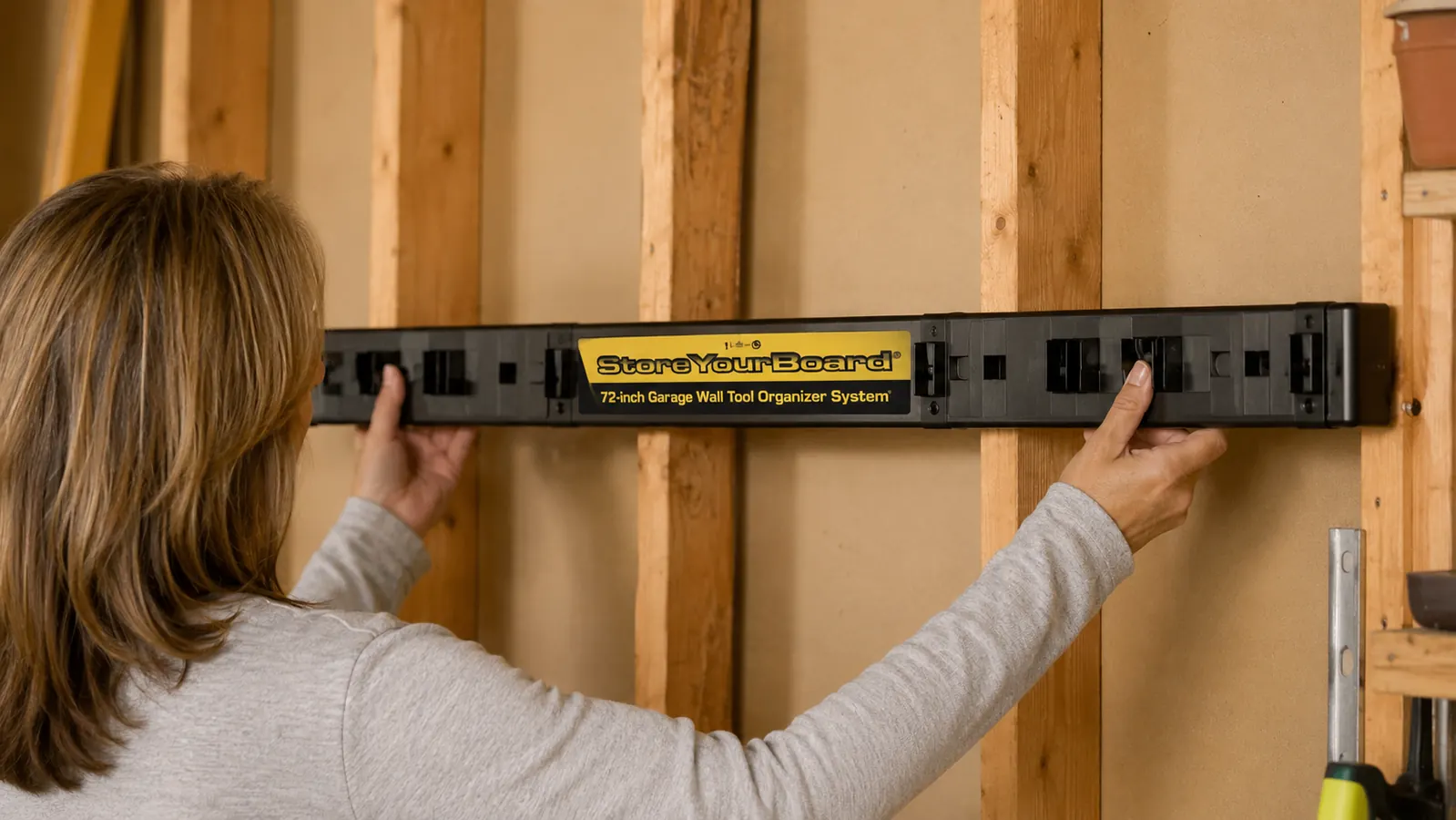 Woman mounting the StoreYourBoard 72-inch tool organizer on a garage wall stud